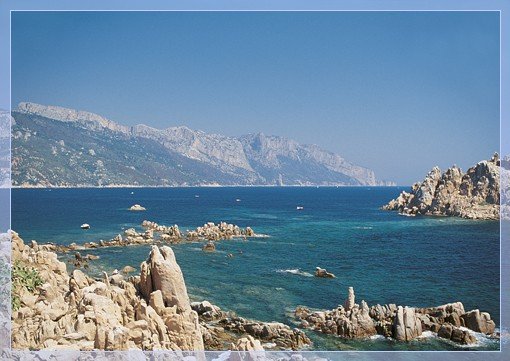 Costa rocciosa con mare e monti lontani.