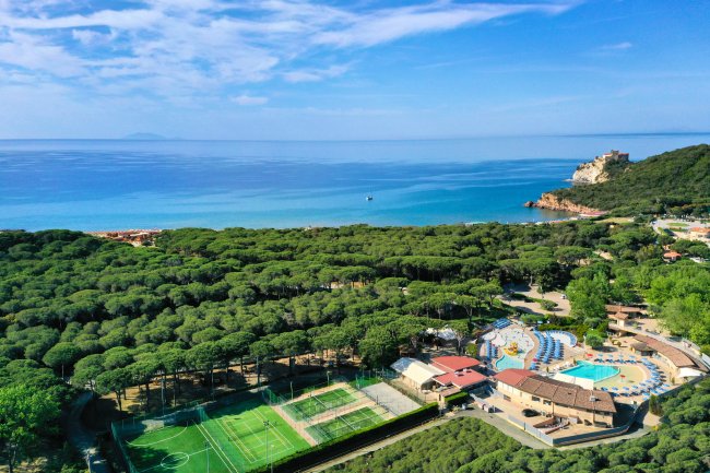 Vista aerea di un resort con piscine e campi sportivi vicino al mare.
