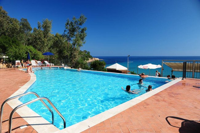 Piscina all'aperto con vista mare e persone che nuotano.