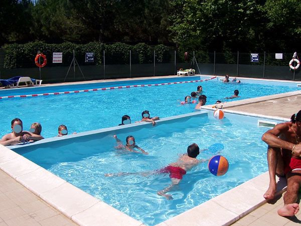 Persone nuotano e giocano con palloni in una piscina all'aperto.