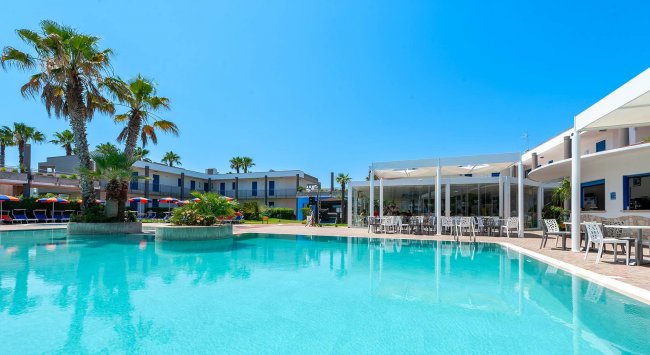 Piscina con palme e sedie a bordo, cielo azzurro.