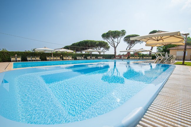 Una piscina azzurra con lettini e ombrelloni.