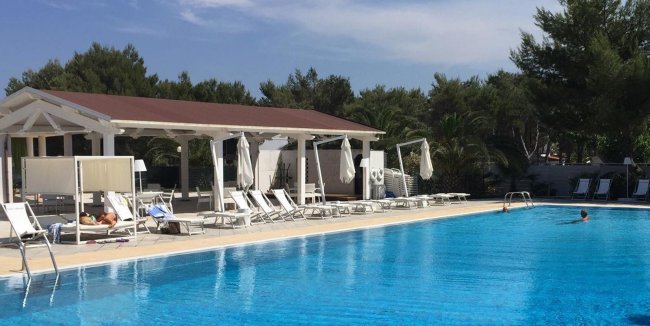 Piscina all'aperto con lettini e tettoia bianca.