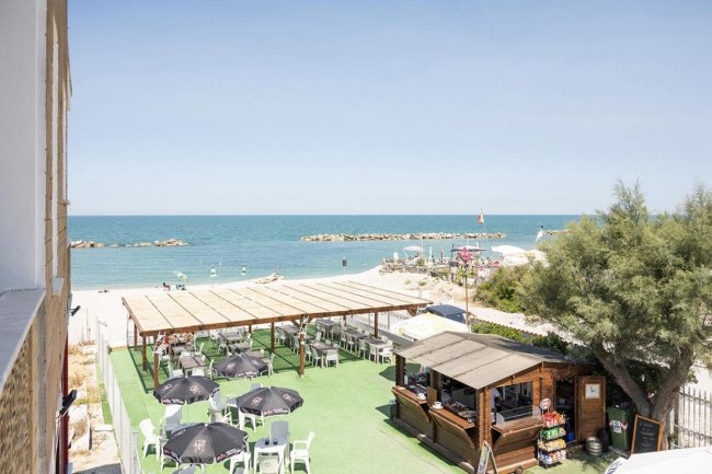 Spiaggia con terrazza, ombrelloni neri e vista mare.