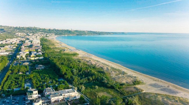 Vista aerea di una costa con spiaggia e mare blu.