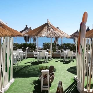 Area esterna con ombrelloni di paglia e tavoli vicino al mare.