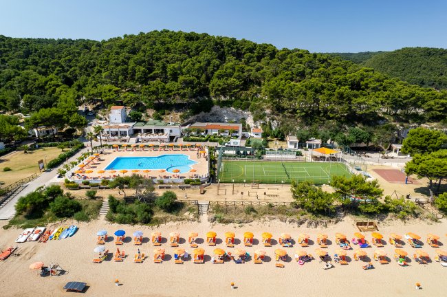 Resort sulla spiaggia con piscina, campo da tennis e lettini.