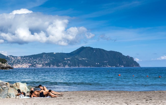 Spiaggia con persone e montagne sullo sfondo.