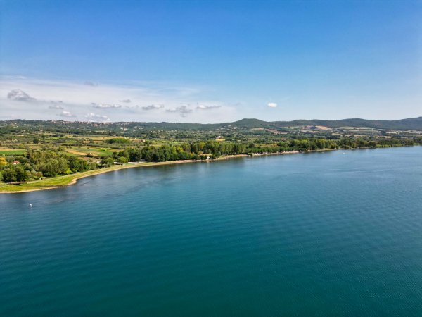 Lago calmo con colline verdi e cielo chiaro.