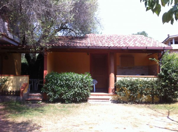 Una casetta con veranda e cespugli davanti.