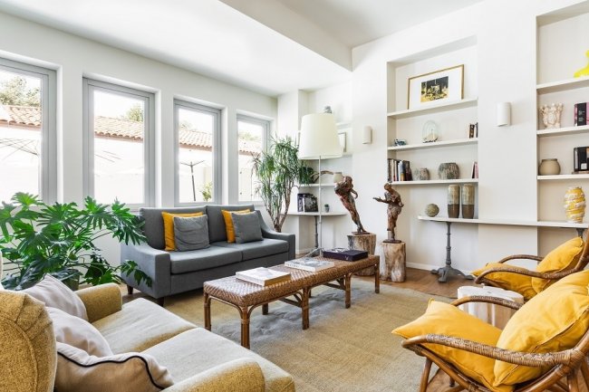 Salotto luminoso con divani, cuscini gialli e piante.