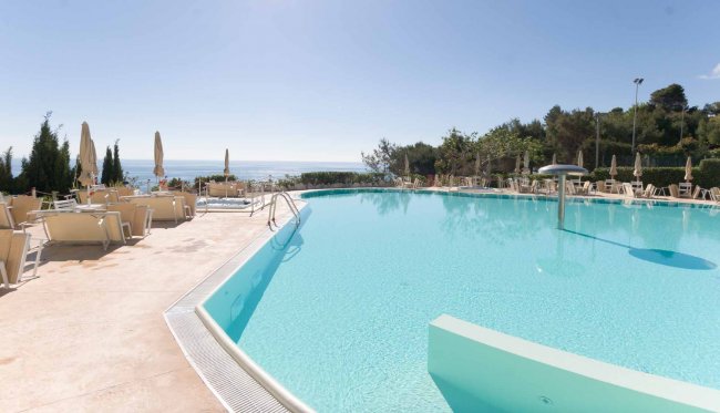 Piscina all'aperto con vista mare e lettini.