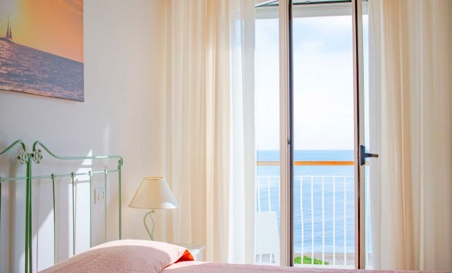 Camera luminosa con vista mare e tende bianche.
