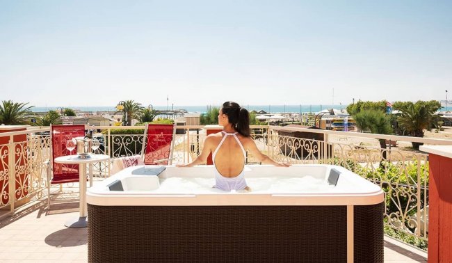 Una donna in una vasca idromassaggio su una terrazza vista mare.