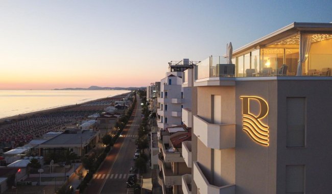 Edifici su lungomare al tramonto, logo 