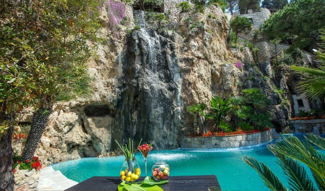 Cascata in piscina circondata da piante e fiori variopinti.