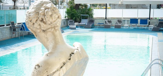 Piscina con statua e lettini attorno.