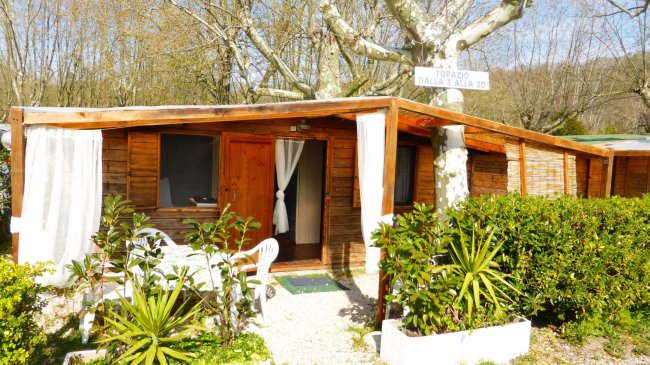 Bungalow in legno circondato da piante verdi, portico con sedie.