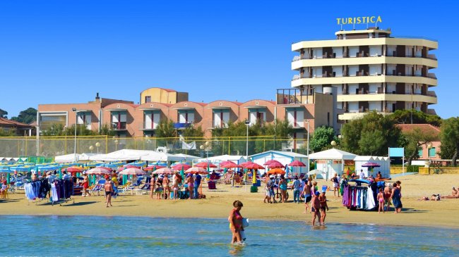 Spiaggia affollata con ombrelloni e un edificio sullo sfondo.