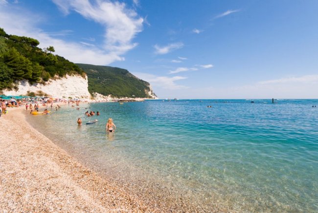 Spiaggia con mare cristallino e scogliere verdi.