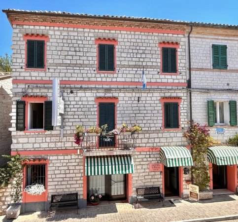Edificio in pietra con tende a righe e balcone fiorito.