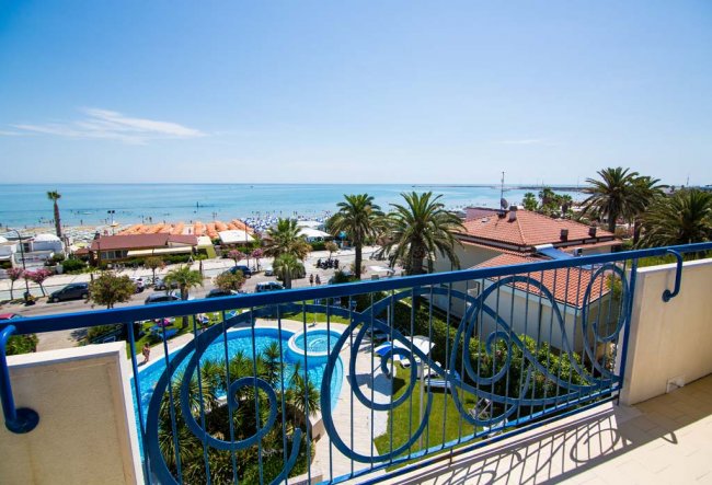 Vista dal balcone sul mare e piscina circondata da palme.
