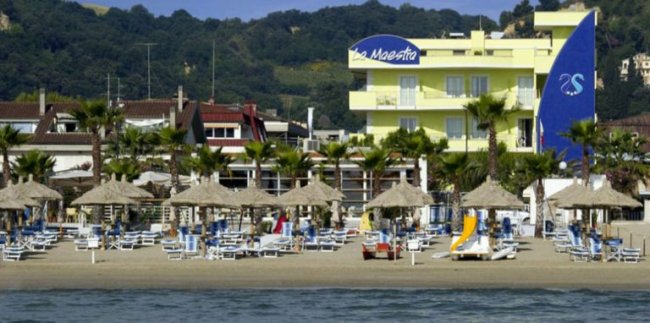 Spiaggia con ombrelloni di paglia e un hotel giallo in background.