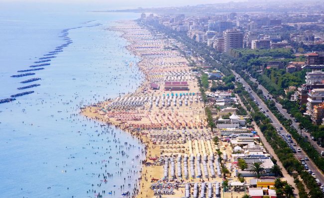 Spiaggia affollata vista dall'alto con ombrelloni e mare azzurro.