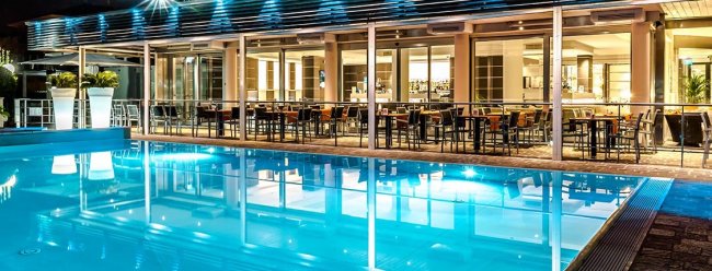 Piscina illuminata di notte accanto a un ristorante.