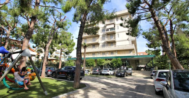 Edificio circondato da alberi e auto parcheggiate.