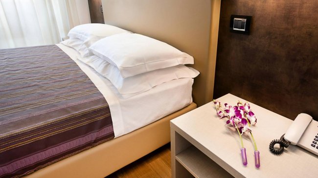 Letto elegante con lenzuola bianche e orchidee sul comodino.