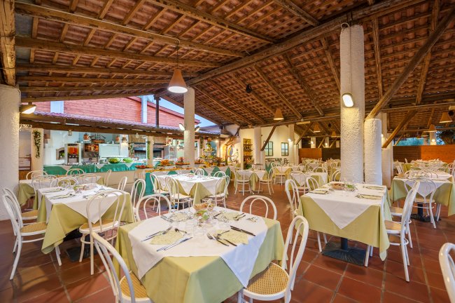 Ampia sala ristorante con tavoli apparecchiati, sedie bianche e tetto di legno.