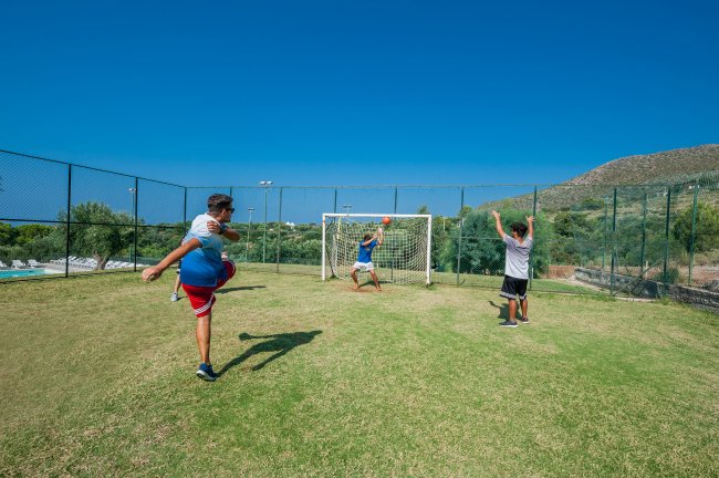 Tre persone giocano a calcio vicino a una porta su un campo verde.