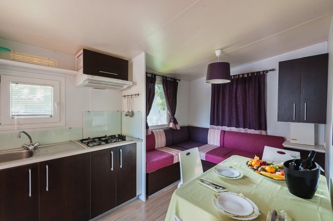 Interno di una casa mobile con cucina, tavolo apparecchiato e divano con tende viola.