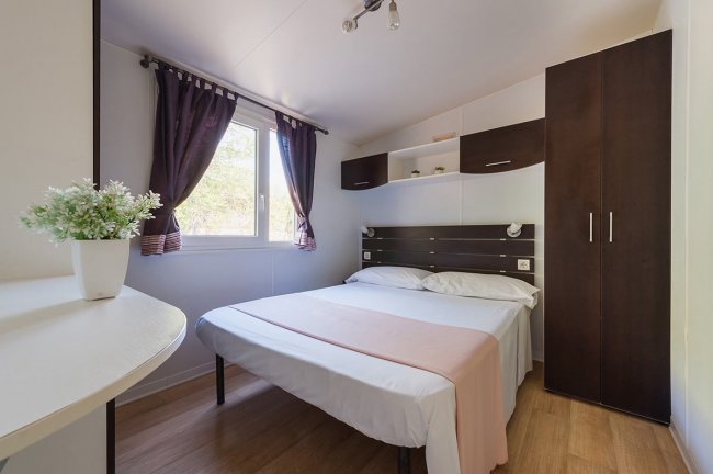 Camera da letto con letto matrimoniale, armadio scuro e finestra con tendaggi viola.