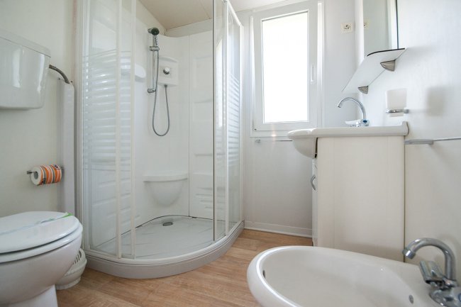 Un bagno moderno con cabina doccia arrotondata, wc, lavabo e bidet, pavimento in legno chiaro.