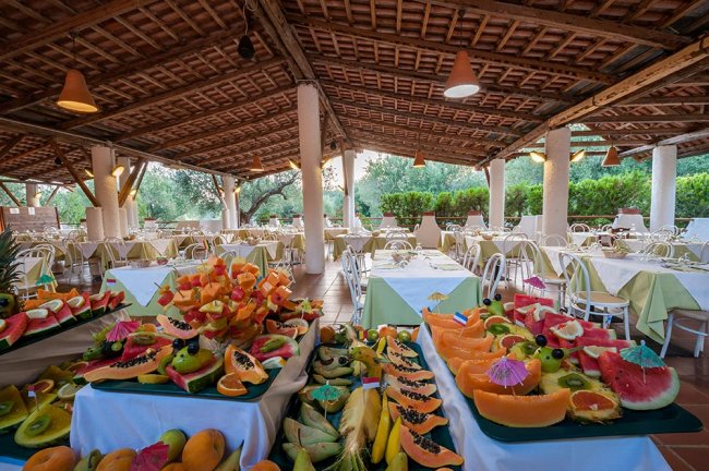 Una sala da pranzo all'aperto con tavoli apparecchiati e un buffet di frutta colorata.