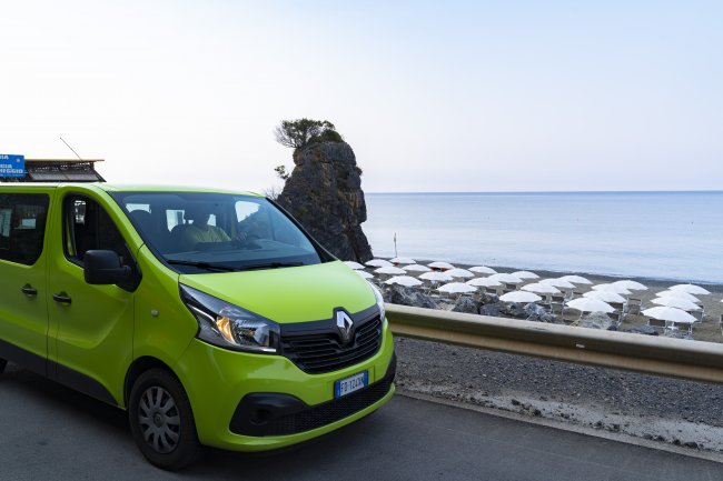 Furgone verde Renault vicino a una spiaggia con ombrelloni bianchi.