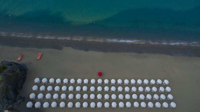 Vista dall'alto di una spiaggia con file di ombrelloni bianchi e uno rosso al centro.