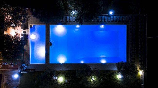 Piscina illuminata di notte, vista dall'alto, con luci che riflettono nell'acqua.