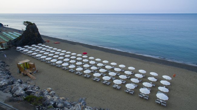 Spiaggia con file di ombrelloni bianchi, mare calmo e un ombrellone rosso in mezzo.