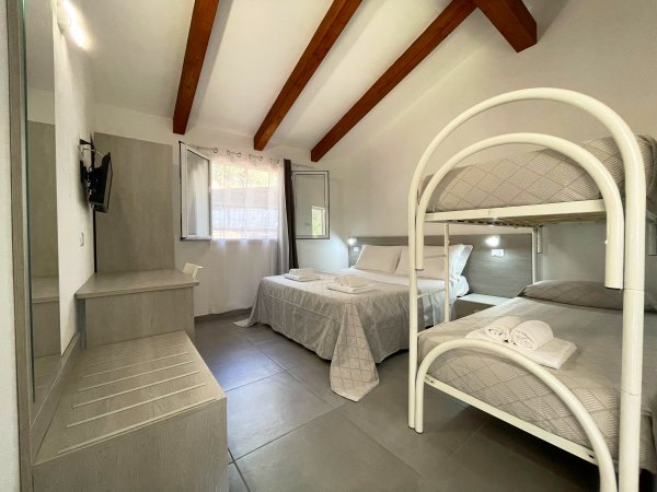Interno di una stanza con letto matrimoniale, letti a castello, travi in legno e TV a parete.