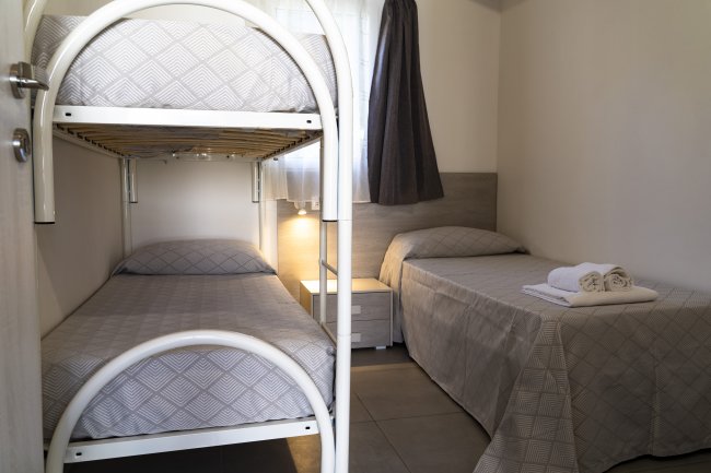 Camera con letto a castello e letto singolo, copertura grigia.