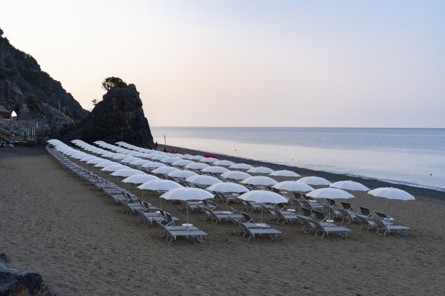 Spiaggia con file ordinate di lettini e ombrelloni bianchi al tramonto.