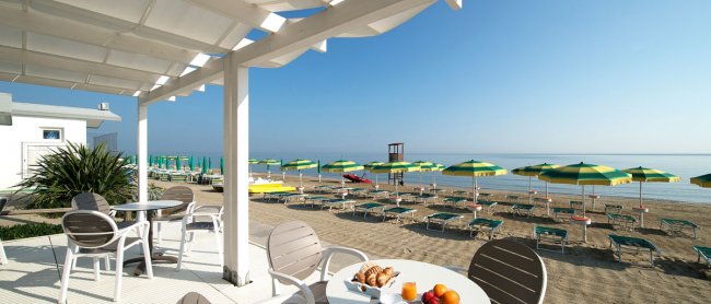 Tavolini all'aperto con vista mare e ombrelloni.