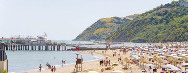 Spiaggia affollata con ombrelloni colorati e un molo.