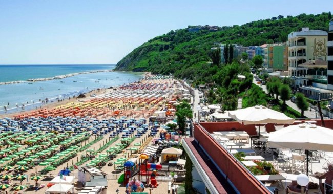 Spiaggia affollata con ombrelloni colorati e un lungomare verde.