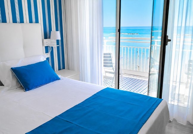 Camera luminosa con letto blu e vista mare dal balcone.
