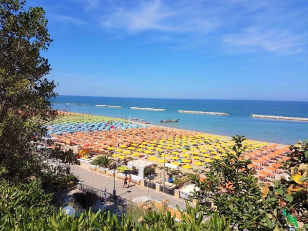 Spiaggia con ombrelloni colorati vista dall'alto, mare blu all'orizzonte.