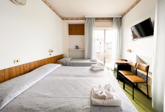 Stanza con due letti singoli, TV a parete, balcone con tende.